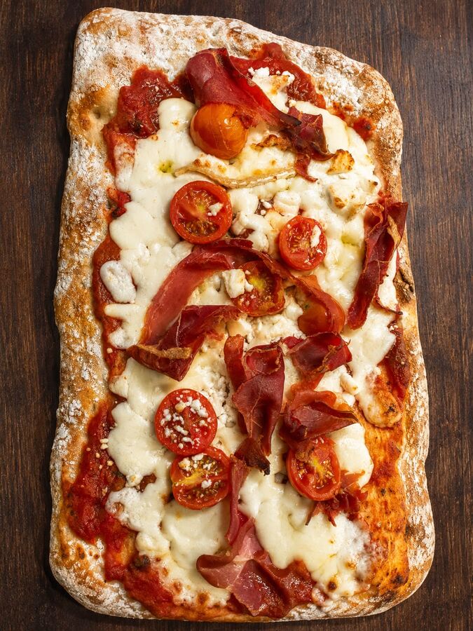 Pizza artesana de masa madre con jamón, mozzarella y tomate cherry